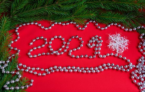 Spruce branches on a red background and numbers 2021 ,lined with silver beads. The concept of a new year.