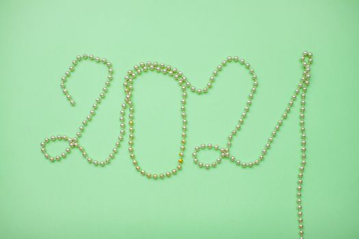 Happy New year 2021 celebration. Inscription 2021 from gold shiny new year beads on a green background