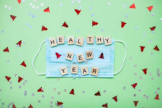 inscription from wooden blocks of a healthy new year on a medical protective mask and on a new year background