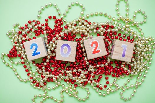 Happy New year 2021 celebration. The inscription 2021 from children's educational wooden cubes on a green background and New Year's decorations: gold and red shiny beads