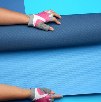 female hand holds a rolled up neoprene sports mat on a blue background, top view