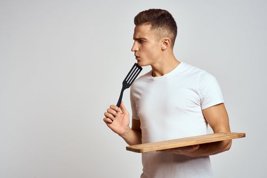 Guy with kitchen tools in hands on a light background cropped view of emotions fun model. High quality photo