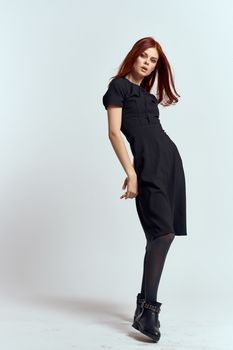 A woman in a black dress on a light background and pantyhose shoes red hair and pose in full growth. High quality photo