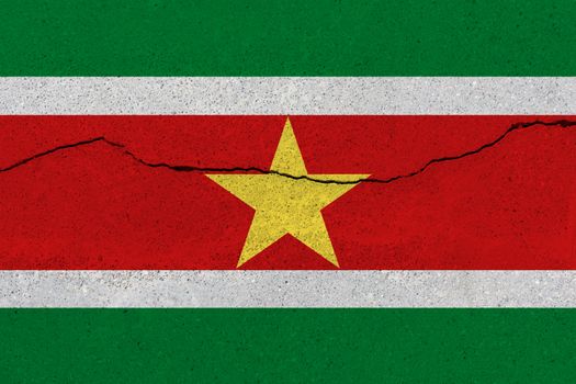 Suriname flag on concrete wall with crack. Patriotic grunge background. National flag of Suriname