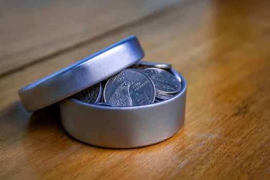 Open silver container filled with coins on a wooden table and an unfocused background