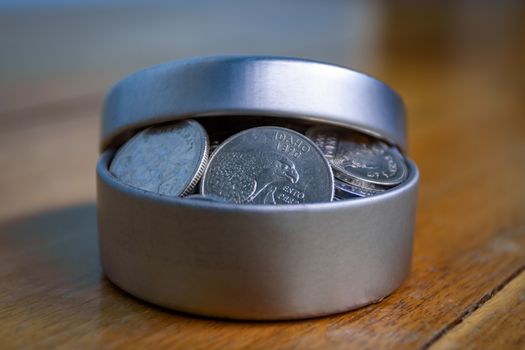 Open silver container filled with coins on a wooden table and an unfocused background