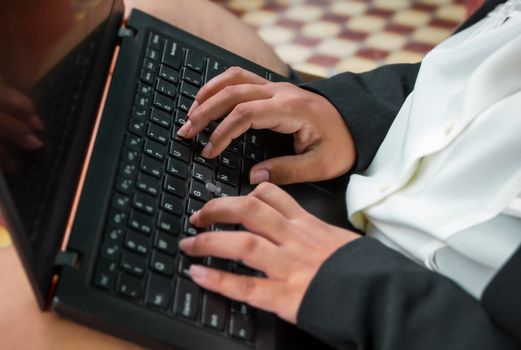 Hands of a Latin woman on the keyboard of a black laptop.