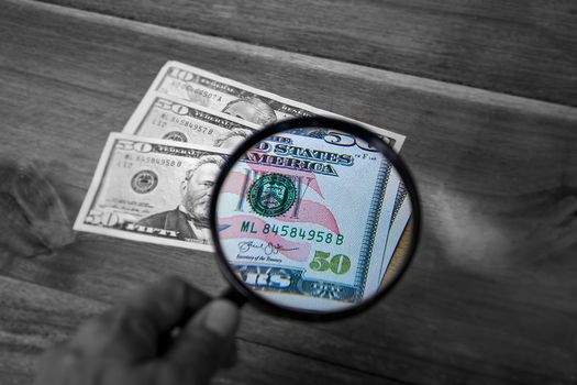 Partial view of a dollar through a magnifying glass. The part of the enlarged image is in color and the rest in black and white