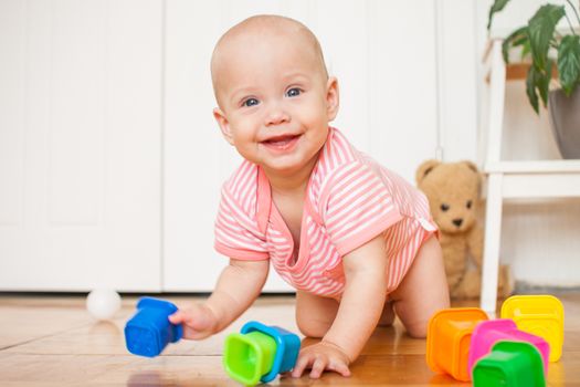 Little baby girl sitting on the floor, crawling and playing with brightly colored educational toys, pyramids