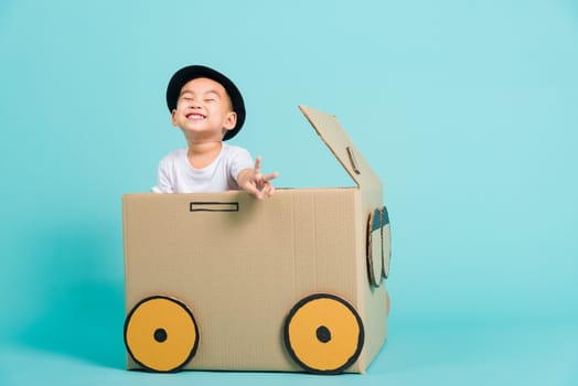 Happy Asian children boy smile in driving play car creative by a cardboard box imagination, summer holiday travel concept, studio shot on blue background with copy space for text