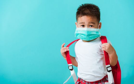 Back to school coronavirus Covid-19 education. Portrait Asian cute little child boy kindergarten wear face mask protective and school bag before going to school, studio shot isolated blue background