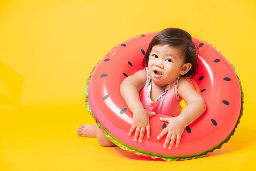 Summer vacation concept, Portrait Asian happy cute little baby girl wear swimsuit sitting in watermelon inflatable ring, Kid have fun sit in inflatable, studio shot isolated yellow background