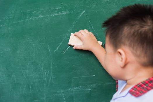 Back to School. Back of Asian cute little child boy kindergarten preschool in student uniform wiping clean or erase chalk on green school blackboard with sponge, First time to school education concept