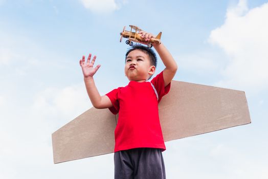 Happy Asian funny child or kid little boy smile wear pilot hat play and goggles with toy cardboard airplane wing flying hold plane toy outdoor against summer blue sky cloud background, Startup freedom