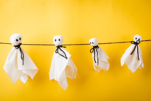 Funny Halloween day decoration party, Full body of baby cute white ghost crafts scary face hanging, studio shot isolated on yellow background, Happy holiday DIY handicraft concept