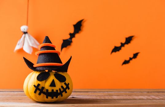 Funny Halloween day decoration party, Cute pumpkin ghost spooky jack o lantern face wear hat, black spider and bats on wooden table, studio shot isolated on an orange background, Happy holiday concept