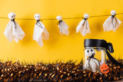 Funny Halloween day decoration party, Cute white ghost crafts scary face hanging on background have only one baby ghost in jar glass, isolated yellow, Happy holiday DIY handicraft concept