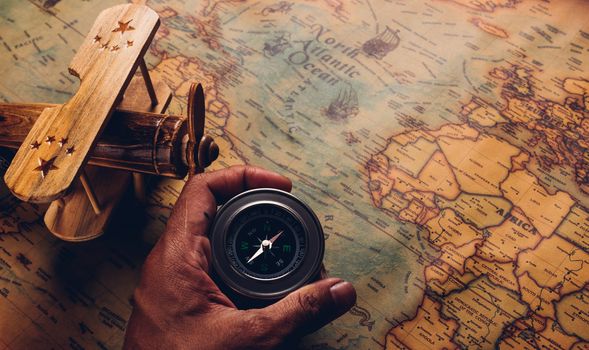 Hand hold old compass discovery and wooden plane on vintage paper antique world map background, Retro style cartography travel geography navigation