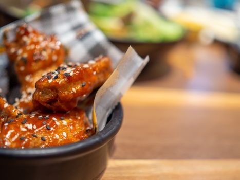 Korean BBQ chicken on a black plate placed on a wooden table and with a blurred background.