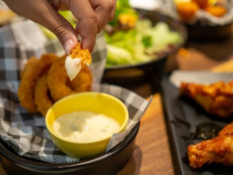 Human hand holding fish finger and dipping on mayonnaise sauce with blurry background.Healthy food or snack for children concept.