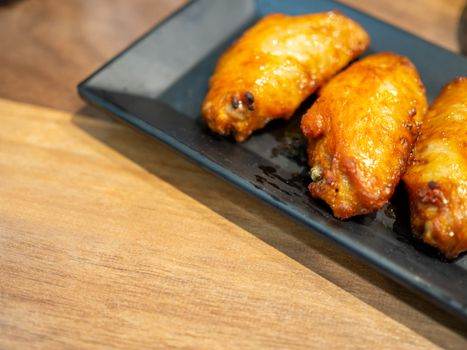 BBQ chicken wings on a black plate and placed on a brown wooden table with copy space.