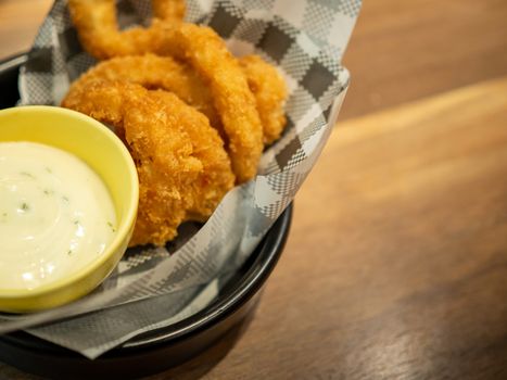 Fish fingers and mayonnaise sauce are on a black plate and on a brown wooden table.