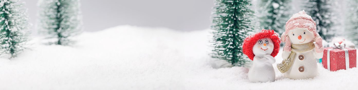 Two small cute snowmen friends with gifts in forest under falling snow