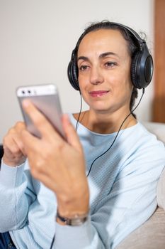 Pretty girl at home on the couch with headphones using smartphone