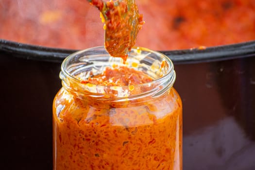 pouring fresly cooked ajvar into the jar with spoon