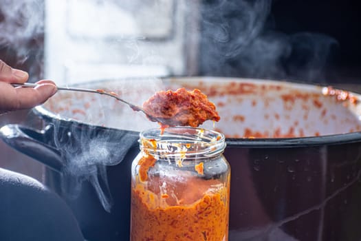 pouring fresly cooked ajvar into the jar with spoon