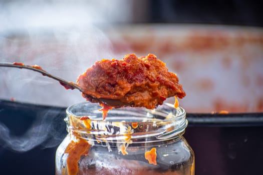 pouring fresly cooked ajvar into the jar with spoon