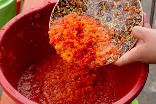 Fresh Ajvar made of tomatoes and paprika on the rustic wooden table. Ajvar with woman hand.