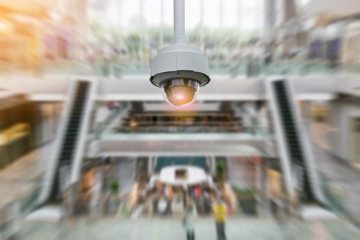 Closeup CCTV security camera on blurred inside shopping mall background.