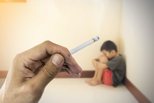 Closeup a cigarette in hand with blurred of the boy hugged her knees in tears in a corner of the room.