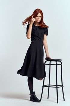 woman high chair indoors full length black dress red hair model boots. High quality photo