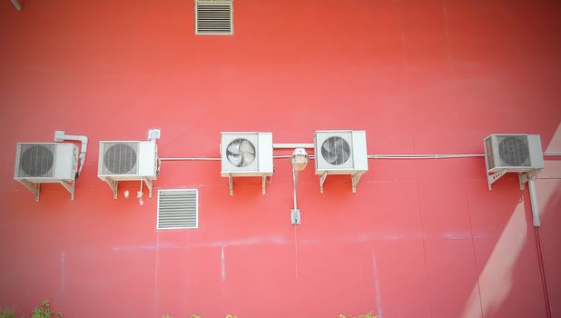 Group of compressor of air conditioner hanging on the red wall.