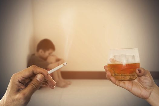 Closeup a cigarette in hand and alcohol  with blurred of the boy hugged her knees in tears in a corner of the room.