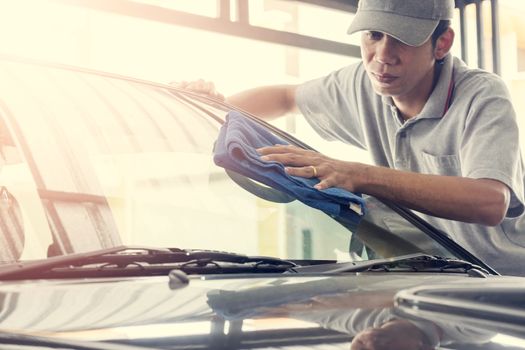 Auto service staff in grey uniform wipe the car glass with microfiber cloth-car detailing and valet concepts.