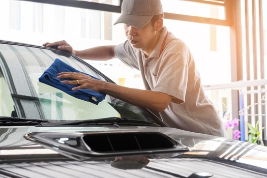 Auto service staff in grey uniform wipe the car glass with microfiber cloth-car detailing and valet concepts.