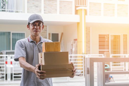 Deliverers in gray uniform stand holding boxes and smiling at customer's front.-Delivery and courier service concepts.