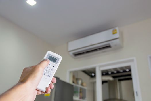 Hand holding the remote to control the air conditioner in the room.