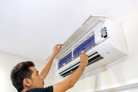 A man is removing the air filter of the air conditioner for cleaning.