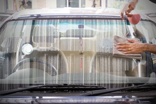 Cleaning staff is using a varnish and microfiber cloth to clean a glass of a car, concept for car care industry.