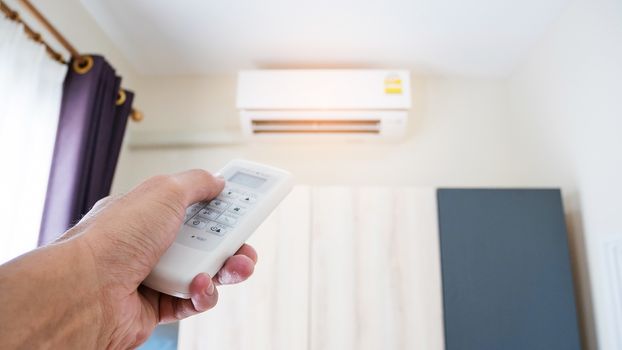 Hand holding the remote to control the air conditioner in the room.