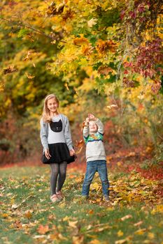 Happy little kids jumping with autumn leaves in the park outdoor