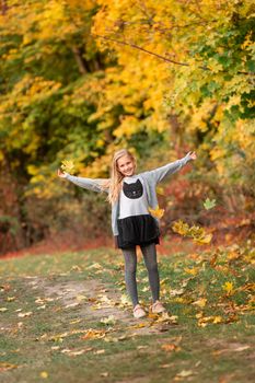 Beautiful little girl jumping with autumn leaves in the park outdoor