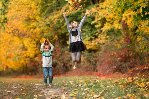 Happy little kids jumping with autumn leaves in the park outdoor