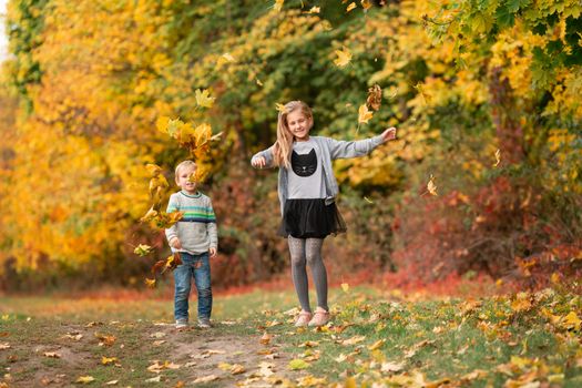 Happy little kids jumping with autumn leaves in the park outdoor