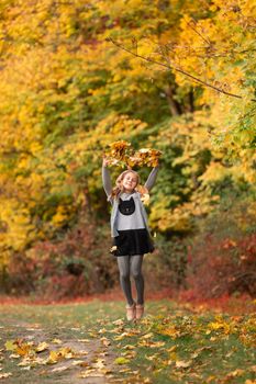 Beautiful little girl jumping with autumn leaves in the park outdoor