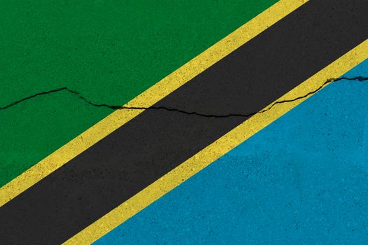 Tanzania flag on concrete wall with crack. Patriotic grunge background. National flag of Tanzania